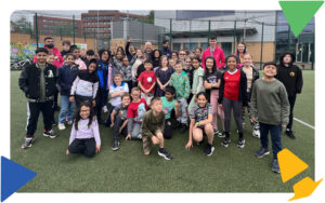 A large group of young people and youth workers smiling on the MUGA pitch